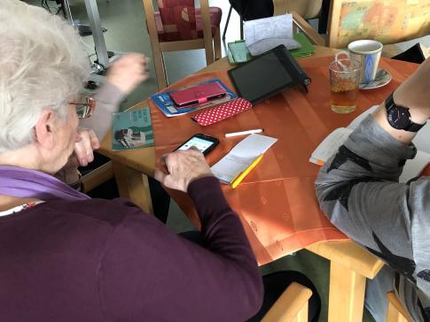 ältere Frau am sitzt am Tisch und bedient ihr Smartphone
