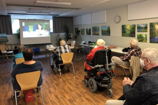 Gemeinschaftsraum im MGH Weimar mit sieben Personen die auf eine Leinwand schauen