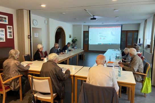 Senioren sitzen im Raum und schauen Richtung Leinwand