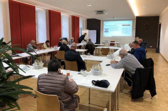 Senioren sitzen im Raum und schauen auf Leinwand