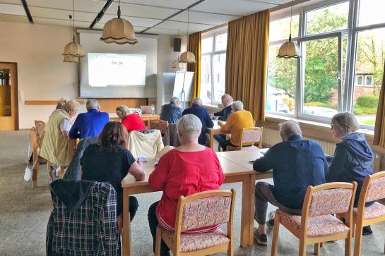 In Oldenburg (Holstein) sitzen Senioren im Raum und schauen auf Leinwand