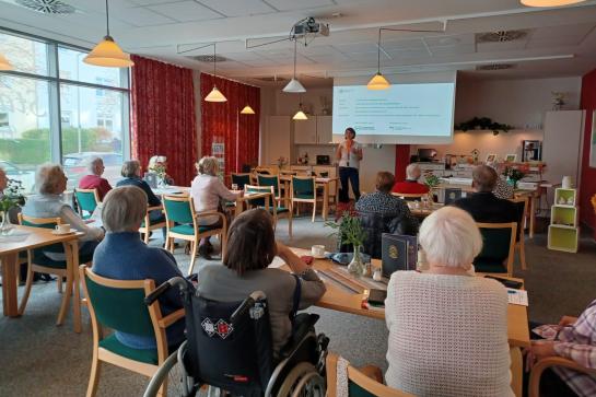 Senioren in Flensburg sitzen im Raum und schauen auf Leinwand