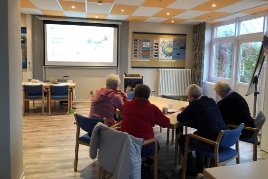 Senioren auf Nordstrand sitzen im Raum und schauen auf Leinwand