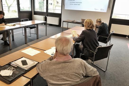 Senioren sitzen am Tisch und schauen auf Leinwand