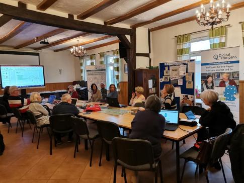 Personen sitzen an einem großen Tisch vor mitgebrachten Laptops