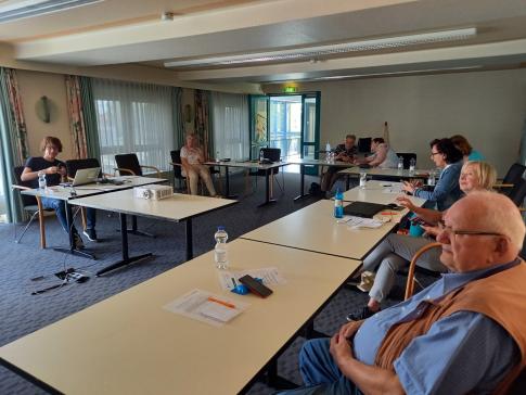 Personen sitzen an Tischen im Raum und blicken zur Leinwand