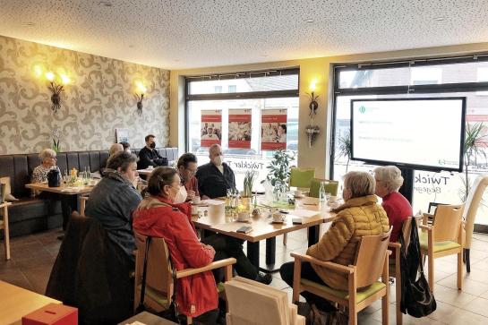 Senioren sitzen an Tischen un dhören einem Vortrag zu