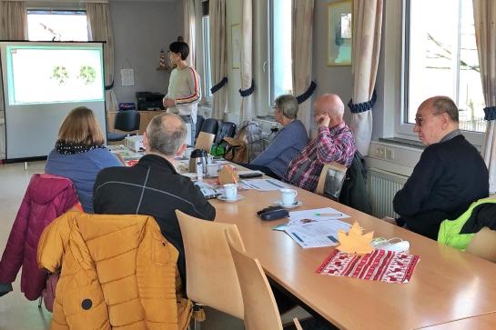 Senioren sitzen im Raum und schauen auf Leinwand