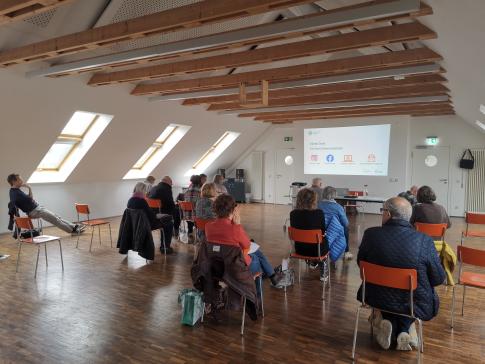 Die Teilnehmenden sitzen im Raum und schauen zur Präsentation an der Wand