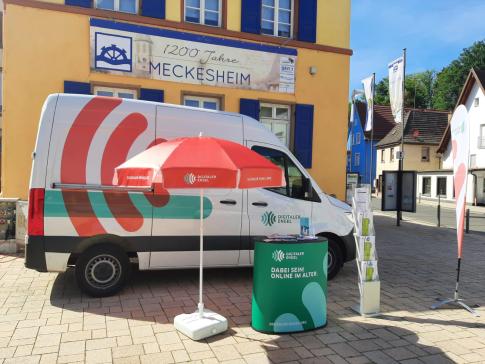 Der Info-Stand mit dem Info-Mobil steht auf dem Rathausvorplatz in Meckesheim. Dahinter ist ein Schild mit der Aufschrift "1200 Jahre Meckesheim" aufgehängt.