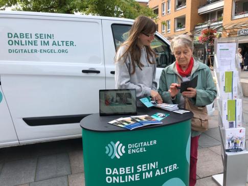 Eine Dame zeigt einer anderen Person etwas auf ihrem Smartphone am Stand des Digitalen Engels.