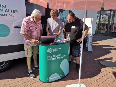 Besuchet stehen vor dem Infomobil und blicken mit unserem Referenten auf einen Laptop