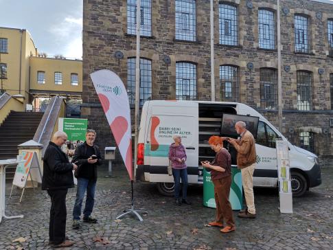 Besucherinnen stehen vor dem Infomobil mir ihren Smartphones und unterhalten sich m