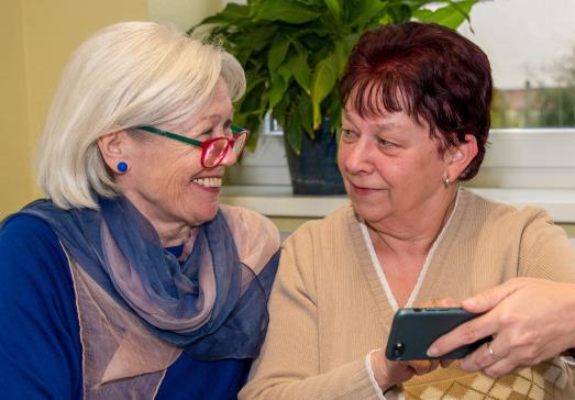 zwei Frauen schauen auf ein Smartphone und lächeln
