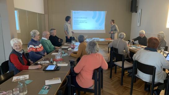 Die Teilnehmenden sitzen im Raum und schauen zu Johannes und Frau Jass, die vor der Leinwand stehen