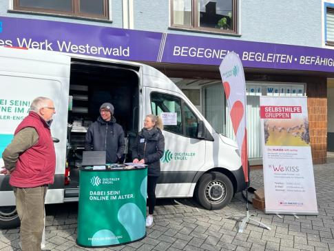 Ein Besucher steht vor dem Infomobil und unterhält sich mit unserem Referenten Johannes und Vanessa Hastrich von der WeKISS