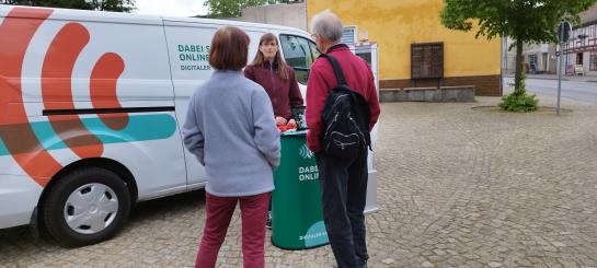 Das Info-Mobil steht auf dem Marktplatz in Mirow. Vor dem Mobil unterhält sich die Referentin vom Digitalen Engel mit einem Ehepaar.