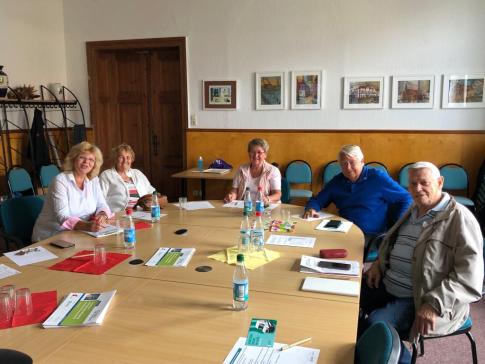 Die Ansprechpartnerin der Stadtbibliothek sitzt mit vier Senior:innen an einem runden Tisch. Auf dem Tisch liegen Smartphones und Broschüren.