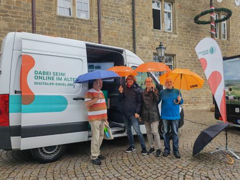 Besucher:innen stehen mit Regenschirmen neben Johannes vor dem Infomobil