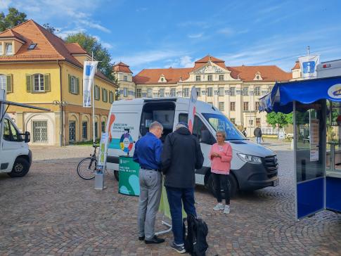 Ein Besucher steht vor dem Infomobil an einem Stehtisch und unterhält sich mit einem Mitglied des Technikcafes Tettnang
