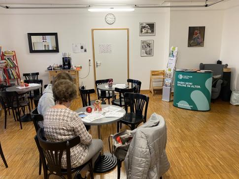 Theresa sitzt mit der Besucherin am Tisch und erklärt ihr Dinge am Smartphone.