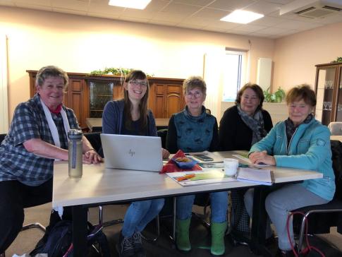 Petra sitzt mit vier Seniorinnen an einem Tisch auf dem ein Laptop steht. Alle fünf Personen schauen und lächeln in die Kamera.