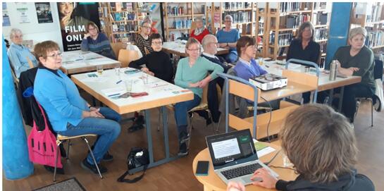 Die Teilnehmenden sitzen an Tischen im Raum und blicken nach vorne zu Johannes der an einem Tisch vor einem Laptop sitzt