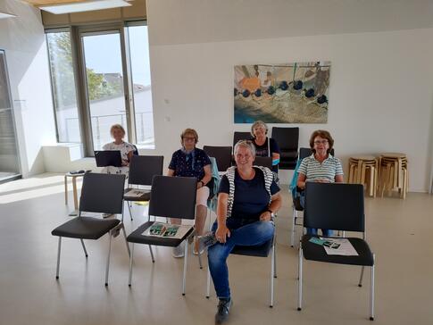 Kooperationspartner Frauke Düßmann und vier Seniorinnen sitzen auf Stühlen und gucken in die Kamera.