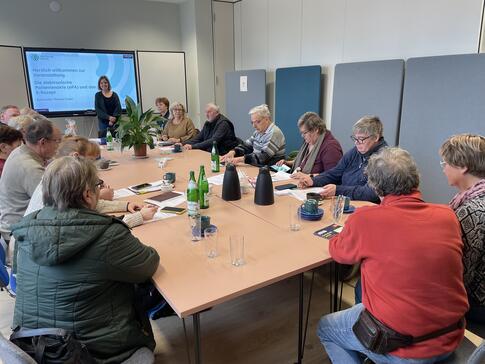 Die Teilnehmenden sitzen zusammen an einem längeren Tisch. Vorne sind Mobilreferentin Theresa und die Titelfolie zum Thema ePA und E-Rezept zu sehen.