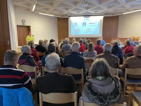 DIe über 30 Teilnehmenden sitzen und schauen auf die Endfolie der Präsentation, die auf einer Leinwand gezeigt wird.