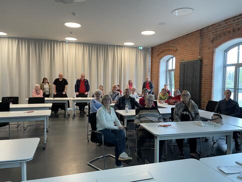 Die Teilnehmenden sitzen und in der hintersten Reihe stehen auch Teilnehmende und lächeln in die Kamera.