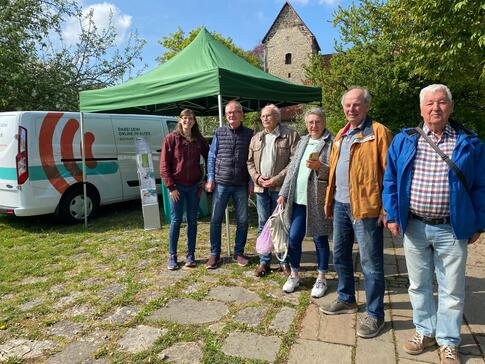 Petra (links) steht mit fünf Senior:innen (vier Männer und eine Frau) vor dem Info-Mobil und einem grünen Pavillon.