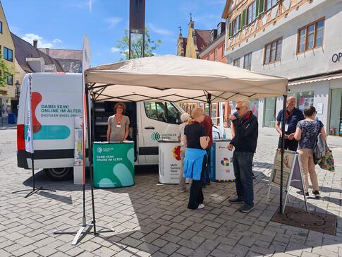Johannes steht vor dem Infomobil und einige andere Personen stehen rechts daneben und unterhalten sich