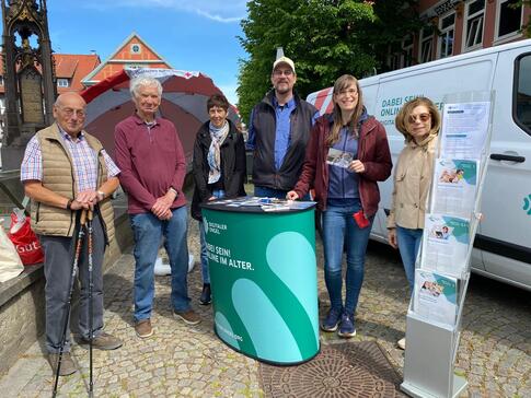 Ein Gruppenfoto mit sechs Personen an dem Info-Stand neben dem Info-Mobil (drei Senior:innen stehen links, daneben von links nach rechts: Herr Beckmann, Petra und Frau Eilert).