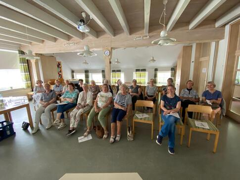 In einem Gemeindehaus sitzen in zwei Stuhlreihen knapp 20 Frauen und blicken nach vorne in die Kamera.