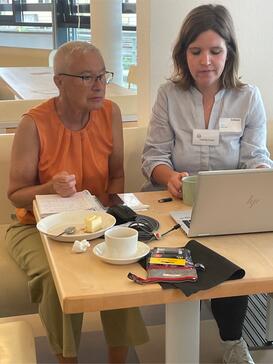 Digitalexpertin Theresa zeigt einer älteren Besucherin Dinge am Laptop.