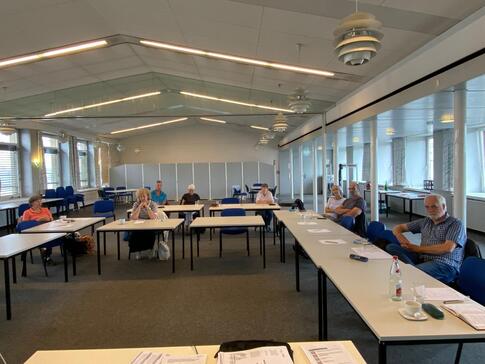 In einem sehr großen Veranstaltungsraum sitzen acht Personen an Tischen in U-Form. Zwei Personen wollten nicht fotografiert werden.