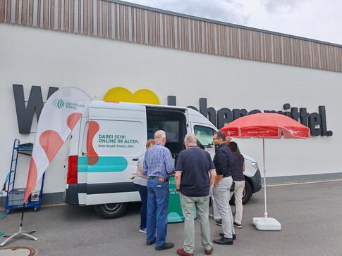 Mehrere Personen stehen vor dem Infomobil, dass vor einem Edeka-Markt platziert wurde.