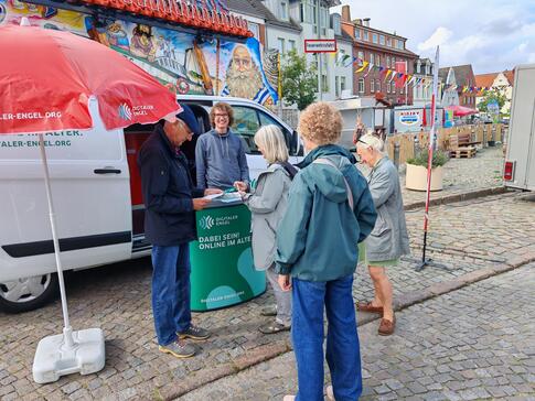 Mehrere Personen stehen vor dem Infomobil und unterhalten sich mit Referent Johannes, der hinter dem Infostand steht.