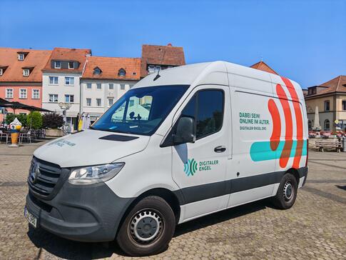 Das Infomobil steht auf einem gepflasterten Platz mit Häusern im Hintergrund.