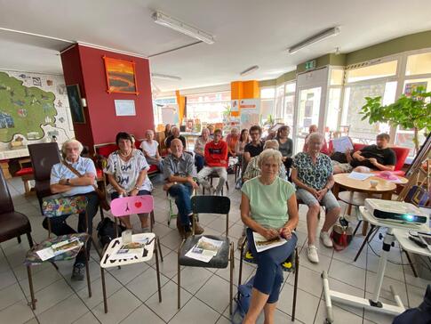 In der kleinen Markthalle in Stendal sitzen Senior:innen und junge Menschen verteilt auf Stühlen im Raum und blicken nach vorne in die Kamera.
