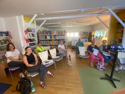 In einem Raum der Stadtbibliothek Seehausen sitzen auf Stühlen verteilt insgesamt sieben Personen. Sie blicken nach vorne in die Kamera. Rechts im Bild steht ein Tisch mit einem Beamer.