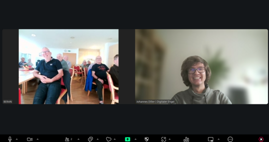 Bildschirmfoto vom Zoom-Fenster, in dem links die Teilnehmenden im Raum sitzend zu sehen sind und rechts Referent Johannes lächelnd in die Kamera blickt.