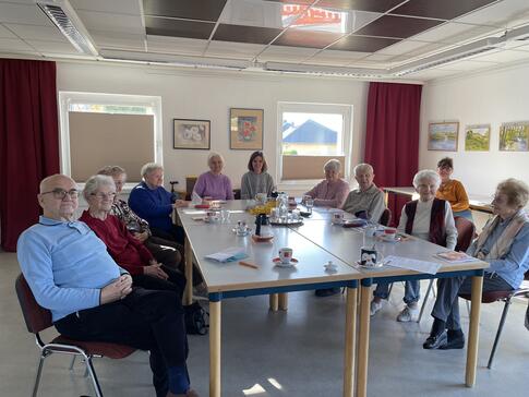 Theresa sitzt zwischen den Teilnehmenden an einem größeren Gruppentisch und lächelt in die Kamera.