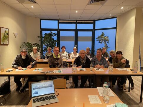 Die Teilnehmenden sitzen in zwei Tischreihen und lächeln in die Kamera.