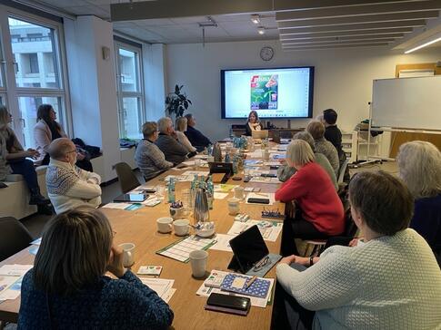 Mobilreferentin Theresa erkl&auml;rt den Teilnehmenden das Lesen der Fernsehzeitung am Laptop. Alle Personen sitzen, zwei Mitarbeiterinnen der Morgenpost stehen links im Bild.