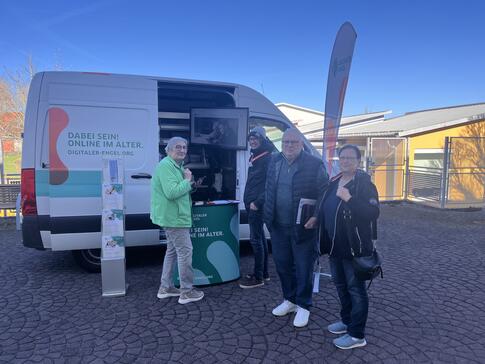 Zwei Frauen und ein Mann stehen neben Mobilreferent Johannes vor dem Infomobil