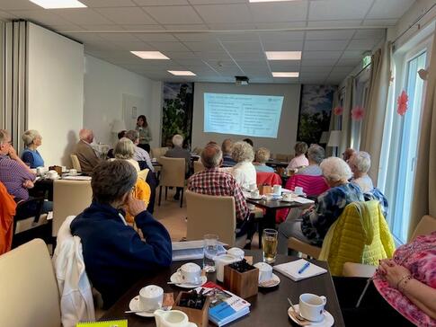 Theresa steht links neben der angezeigten Pr&auml;sentation und stellt vor, was in der ePA gespeichert wird. Die TN sind von hinten zu sehen und schauen zu Theresa.