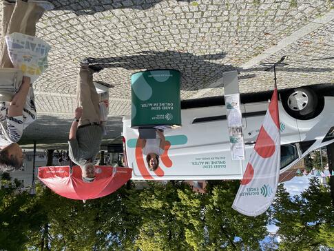 Theresa sowie ein Besucher stehen direkt am Infostand. Eine Besucherin kommt auf die beiden hinzu.