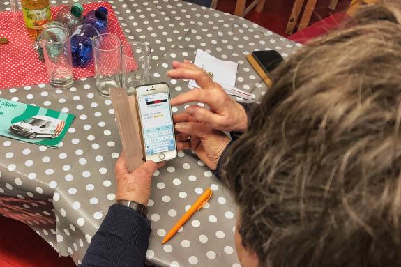 Eine Seniorin sitzt am Tisch und hält ein Smartphone in der Hand